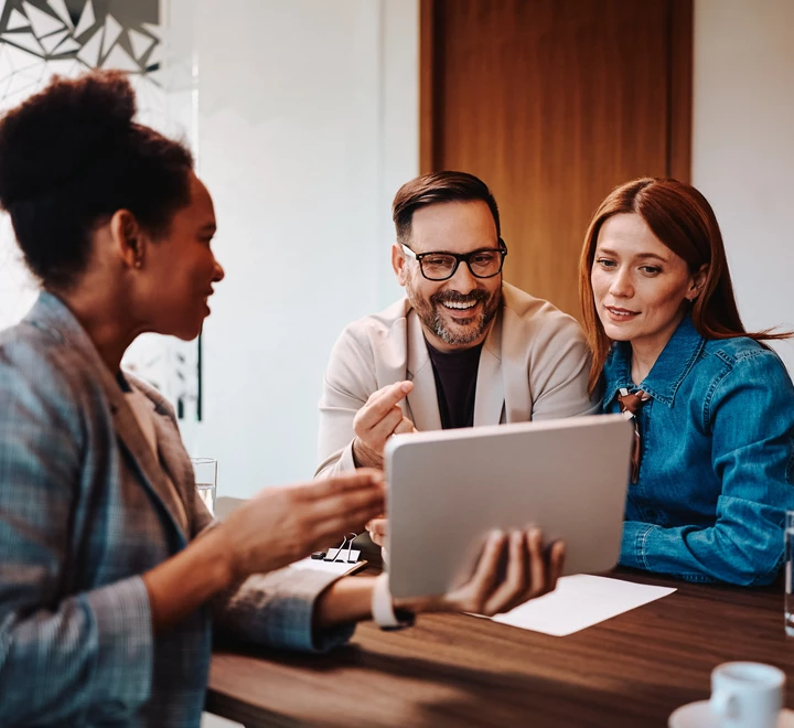 A couple meeting with an advisor who is showing the couple information from her laptop. The meeting is at a table in an office setting. 