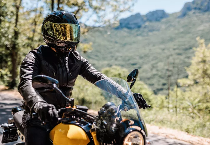 Motorcycle rider in full gear on yellow bike. Green, lush landscape in the background. 