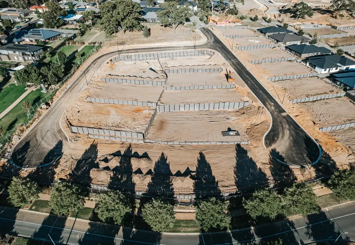 Aerial view of a cleared residential lot with outlined foundations and surrounding roads in a developing neighborhood. 