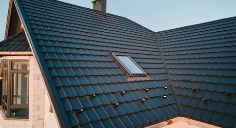 Closeup of attic window on house roof top covered with ceramic shingles. 