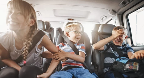 Three playful kids seat belted in the back seat of a vehicle, on a road trip. 