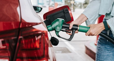 Woman's hands filling up her red car with fuel at a gas station. 