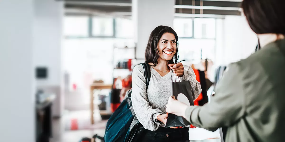 Customer receiving a shopping bag from a retail associate at a checkout counter.