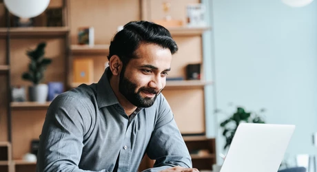 Smiling Middle Eastern professional seated at desk looking at laptop 