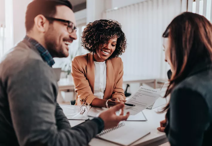 Professional African American woman helping happy couple across her desk with paperwork 