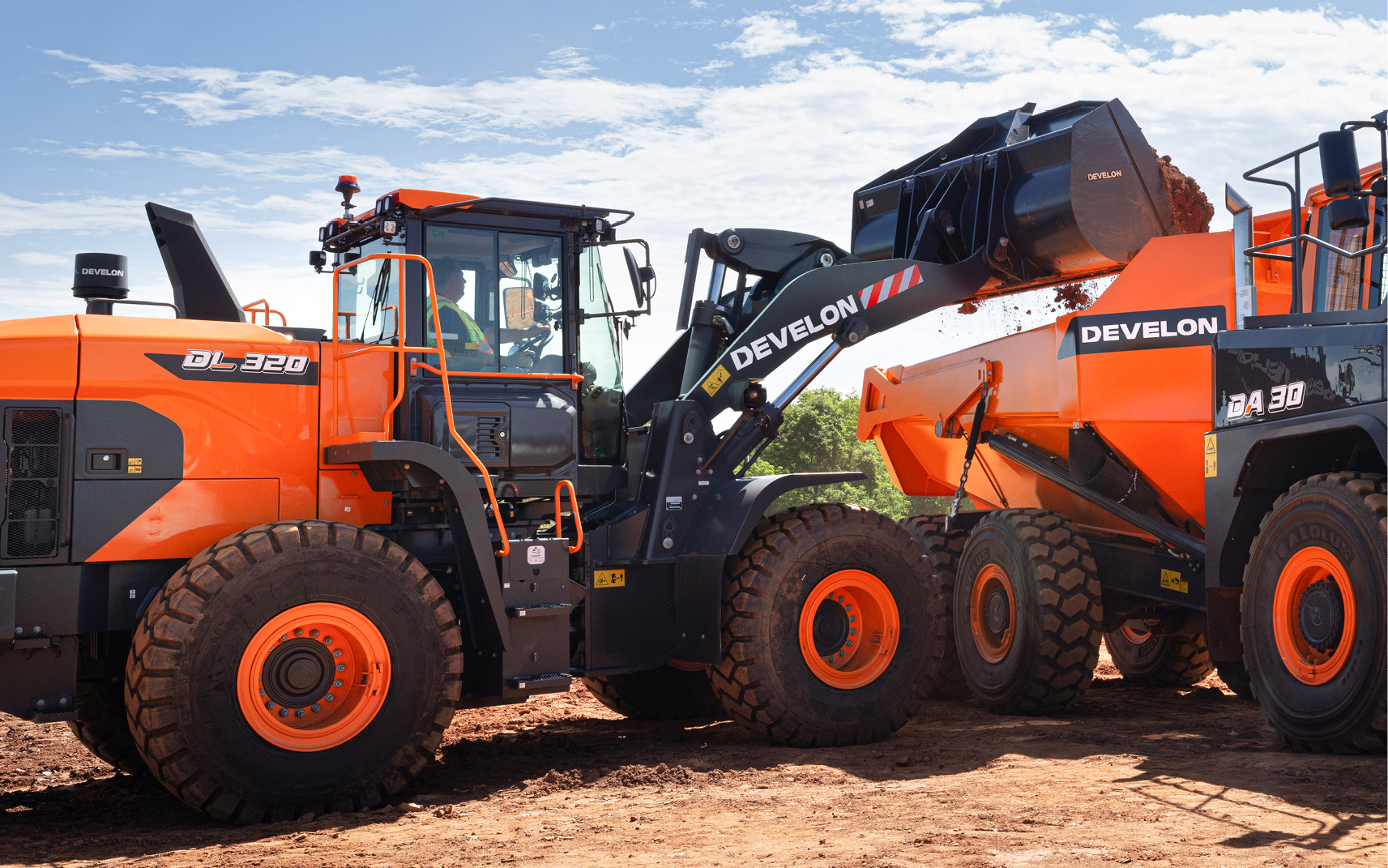 A DEVELON wheel loader empties dirt from a bucket into an articulated dump truck.
