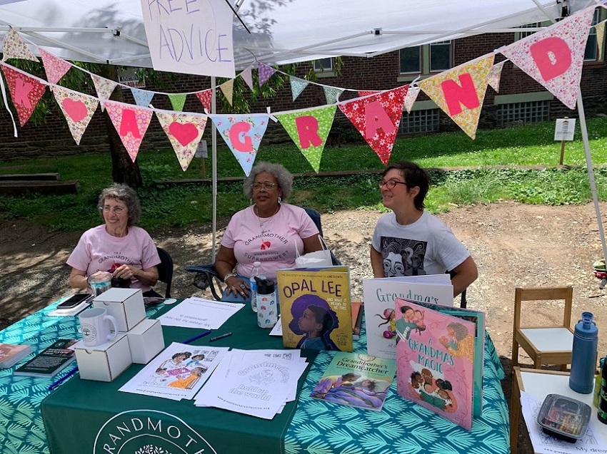 Women sitting at a table under an awning at a public event