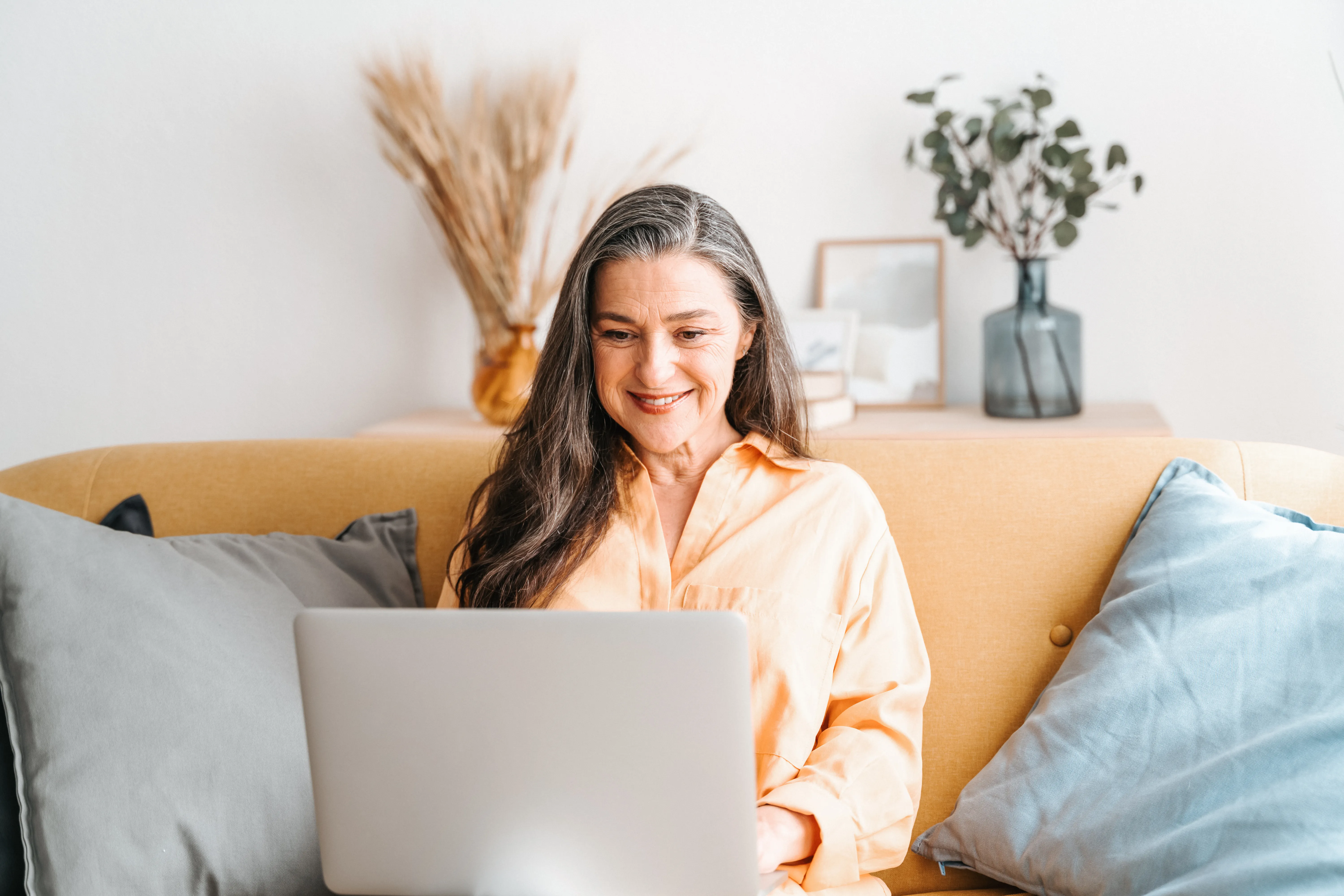 Woman sitting on yellow sofa while using her laptop at home. 