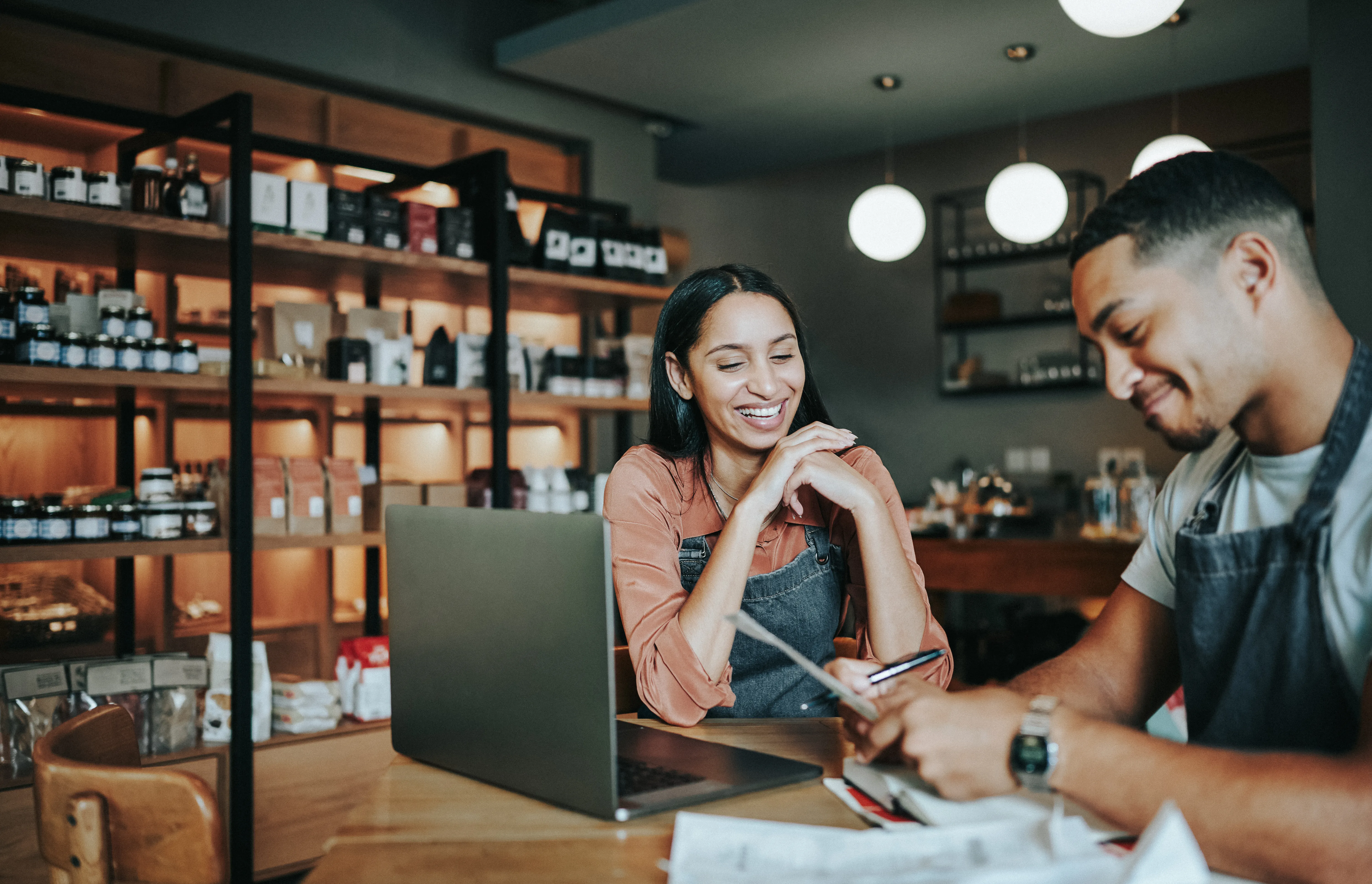 Two business owners going over paperwork and working on a laptop at a table in their shop    