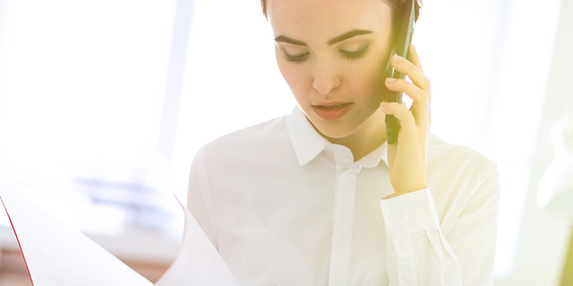 Young girl in the office near the rack and scrolls through the folder with the documents and speaks on the phone.