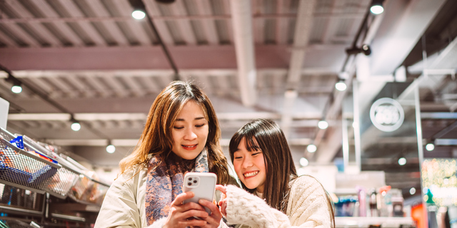 Mother and daughter shopping together using smart phone in store