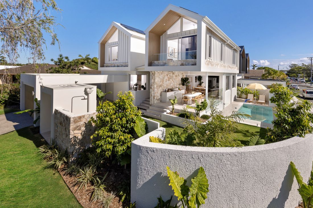 External front of a 2 level white home with driveway and gardens.