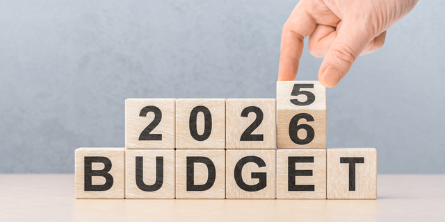 Male hand changing year from 2025 to 2026 on wooden blocks over BUDGET text for financial planning business concept