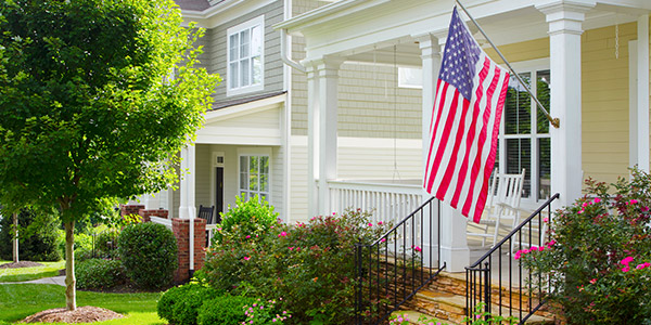 An American flag hangs from the porch of a nice vinyl-sided home