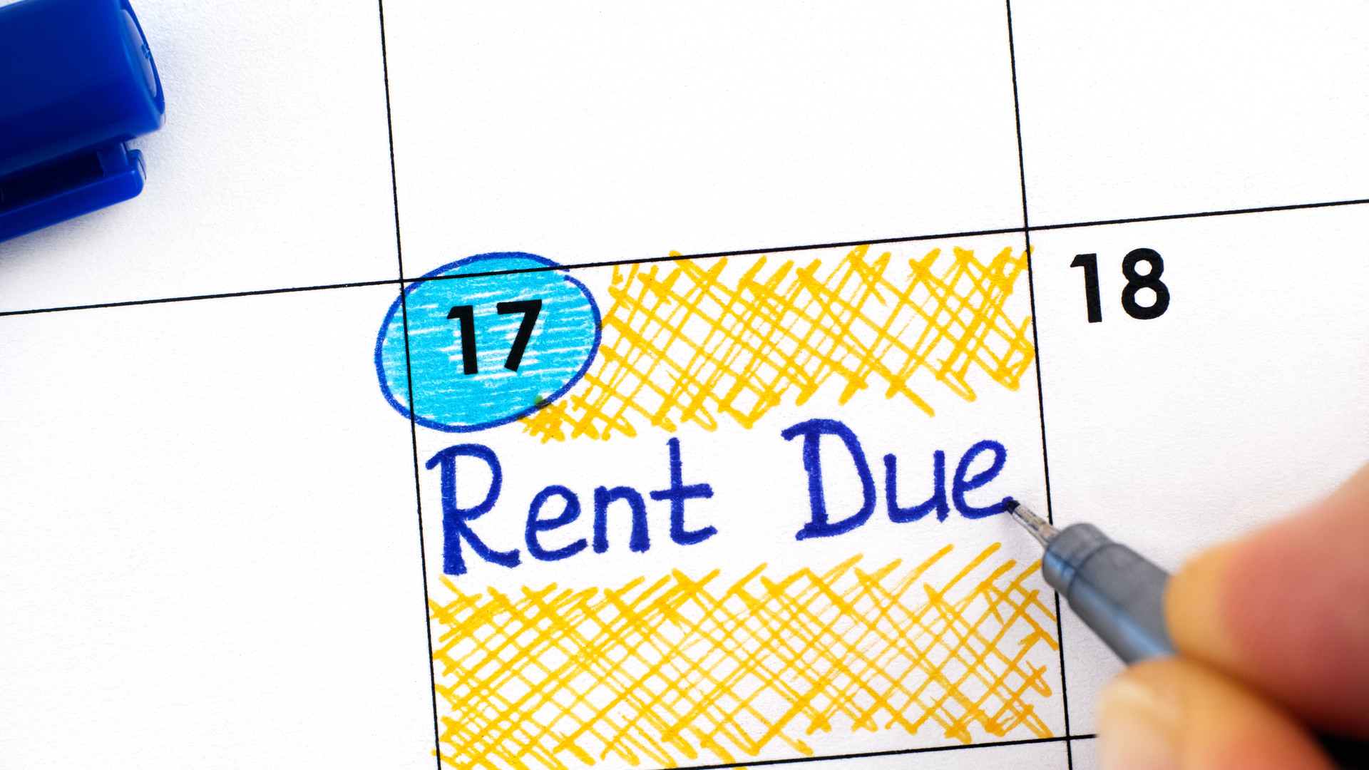 Woman fingers with blue pen writing reminder Rent Due in calendar.