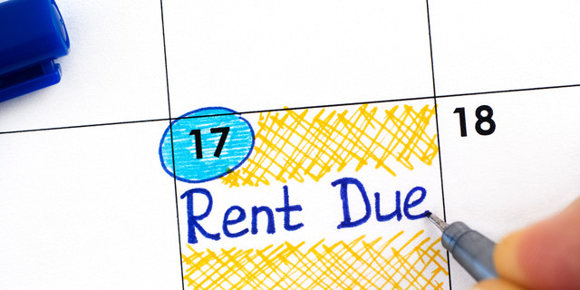 Woman fingers with blue pen writing reminder Rent Due in calendar.