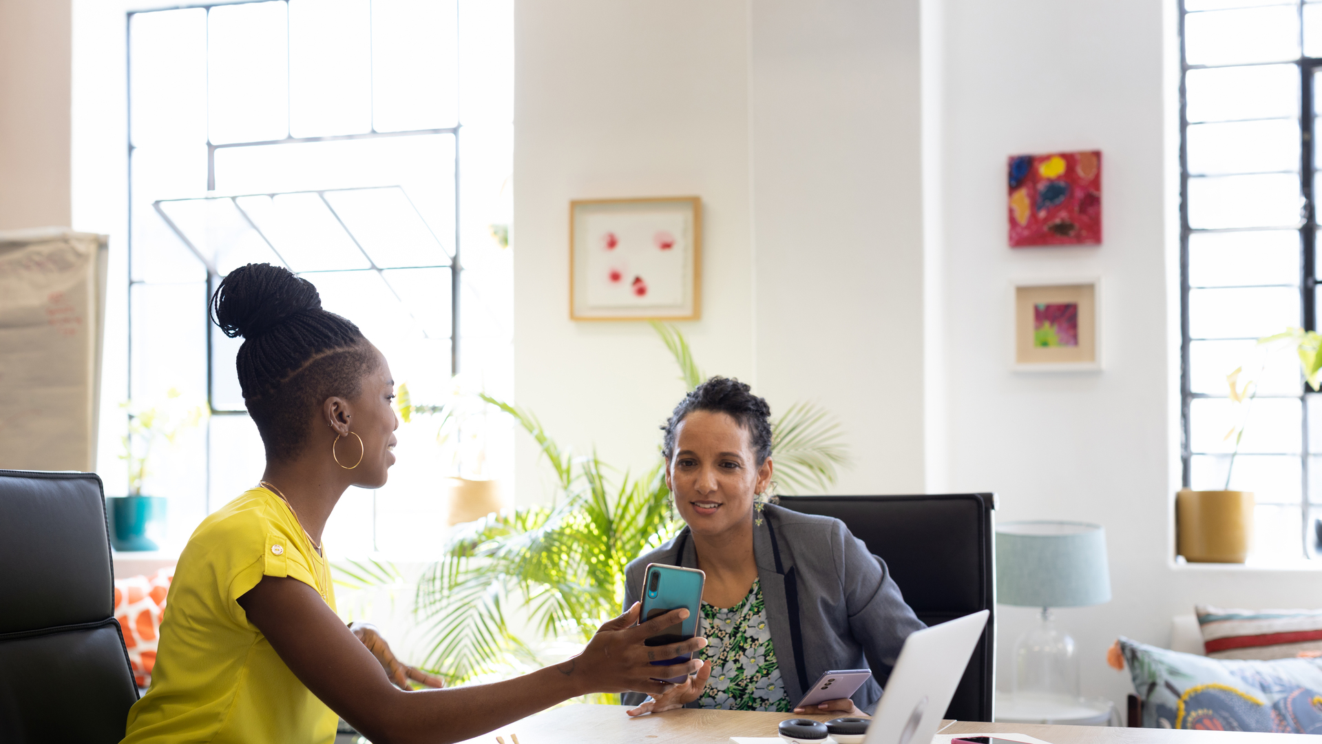 Two female workers sharing images on a smart phone in an office