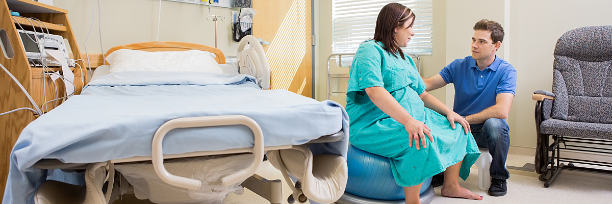 A pregnant patient sits on a rolling ball during labor to allow for movement as she talks with her partner.