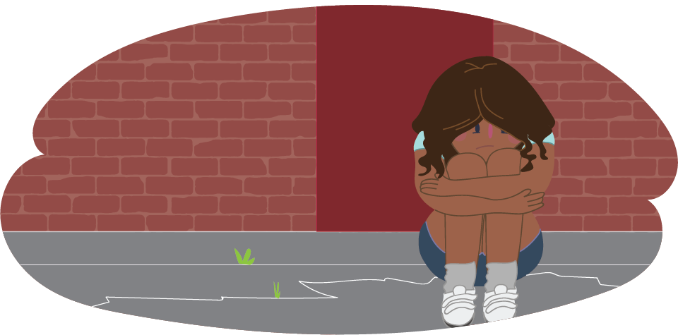 A child hugging their knees while sitting on the ground against a brick wall outdoors.