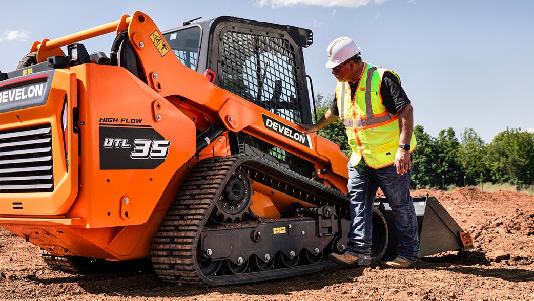 An operator performs a routine maintenance check on a DEVELON DTL35 Compact Track Loader.