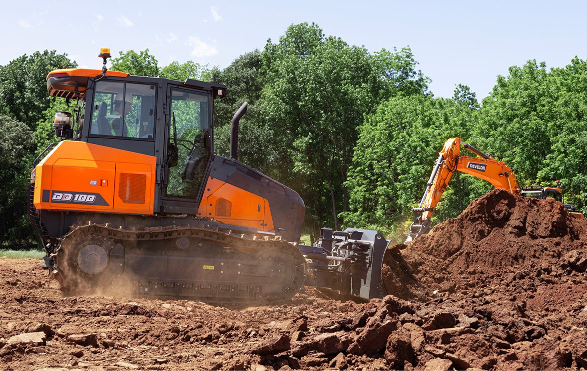 A DEVELON DD100 dozer pushes dirt as a DEVELON excavator works in the background.