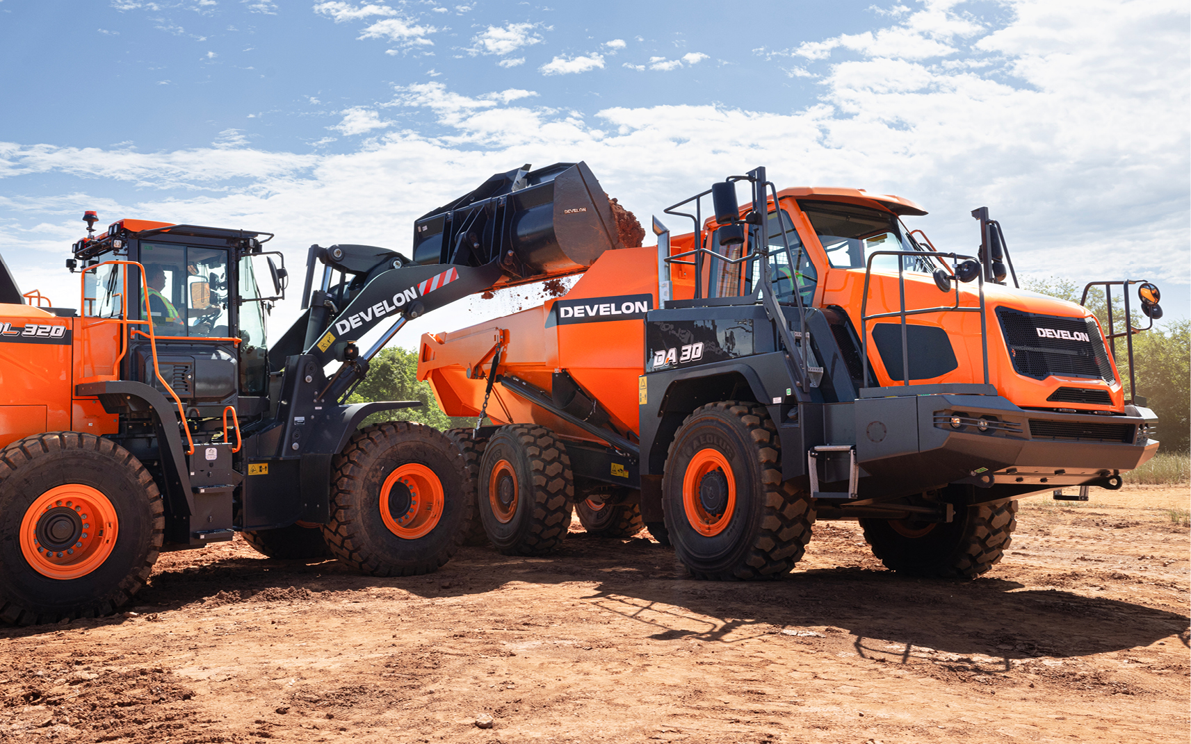 A DEVELON wheel loader empties its bucket of dirt into the bed of an articulated dump truck.