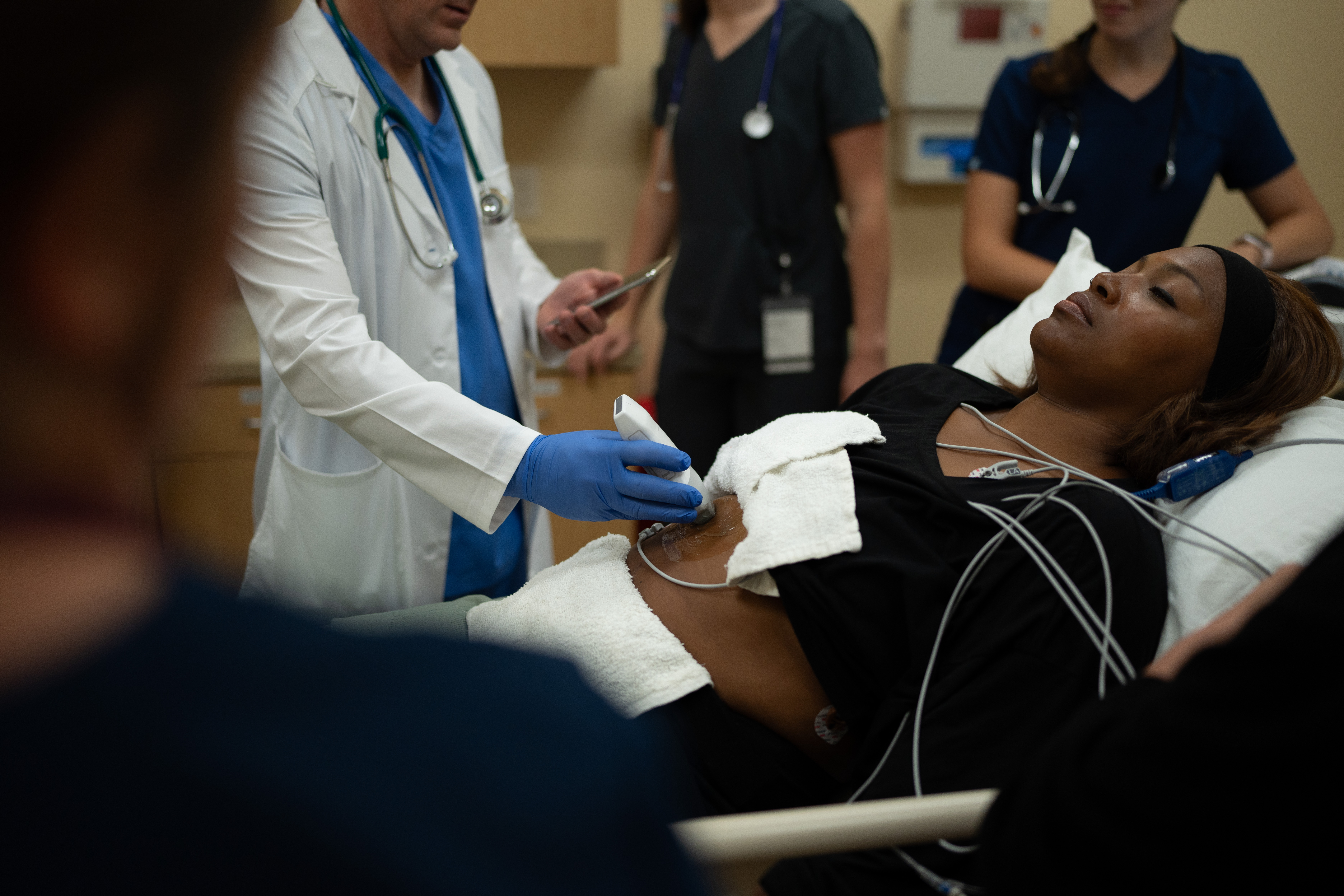 An ED physician uses handheld ultrasound to scan a patient's abdomen.