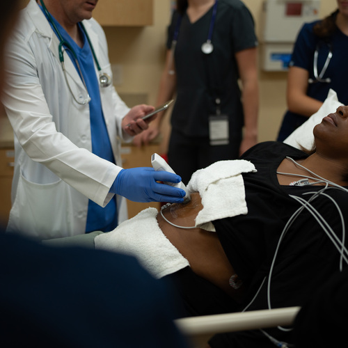 An ED physician uses handheld ultrasound to scan a patient's abdomen.