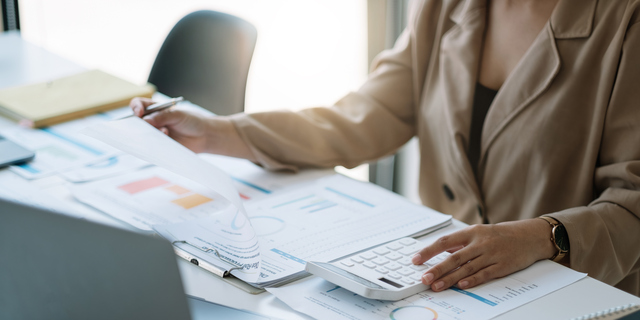 Close up woman planning budget, using calculator and laptop, reading documents, young female checking finances, counting bills or taxes, online banking services