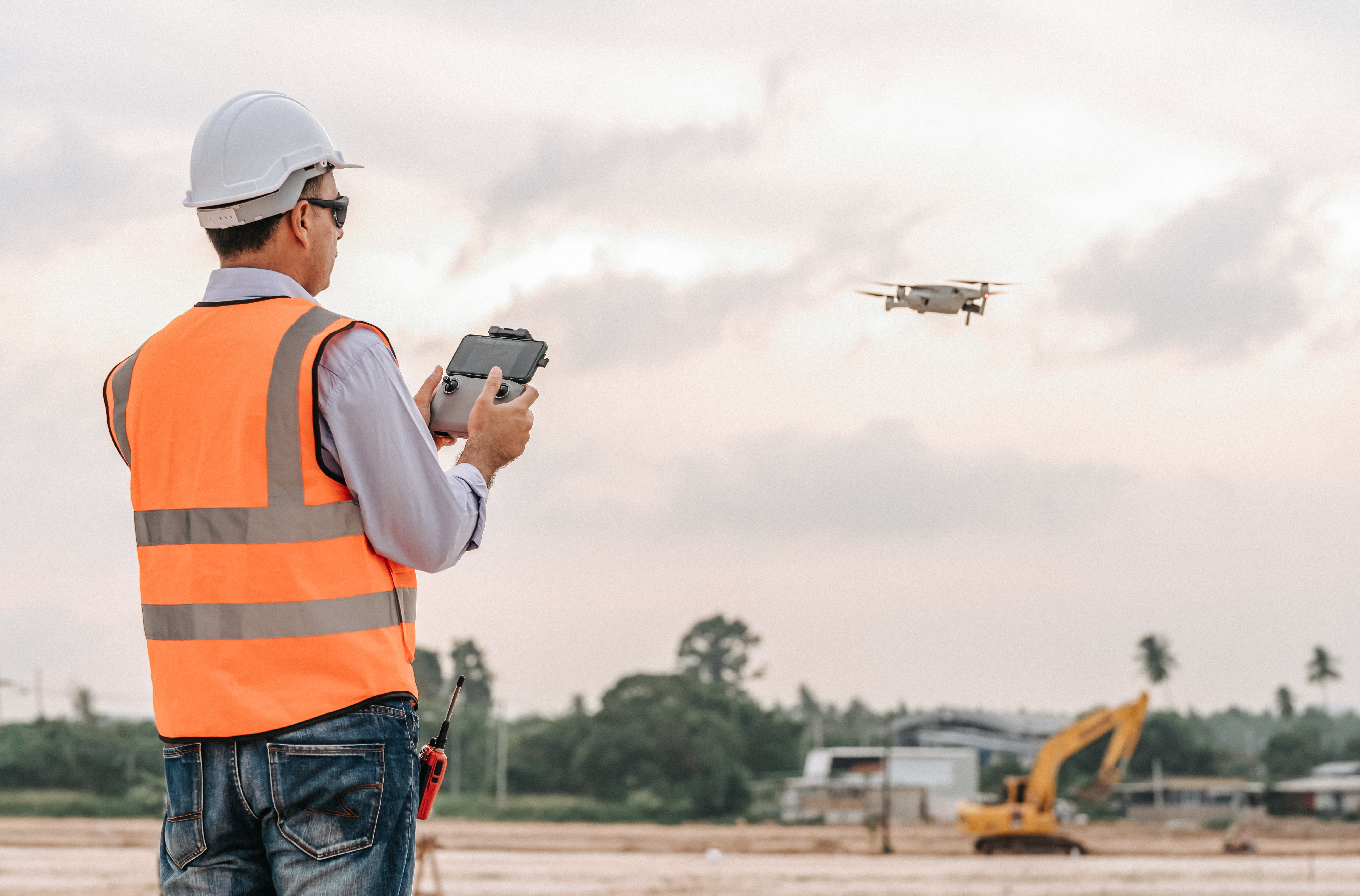Worker in hardhat and high visibility vest in open construction area operating a drone 