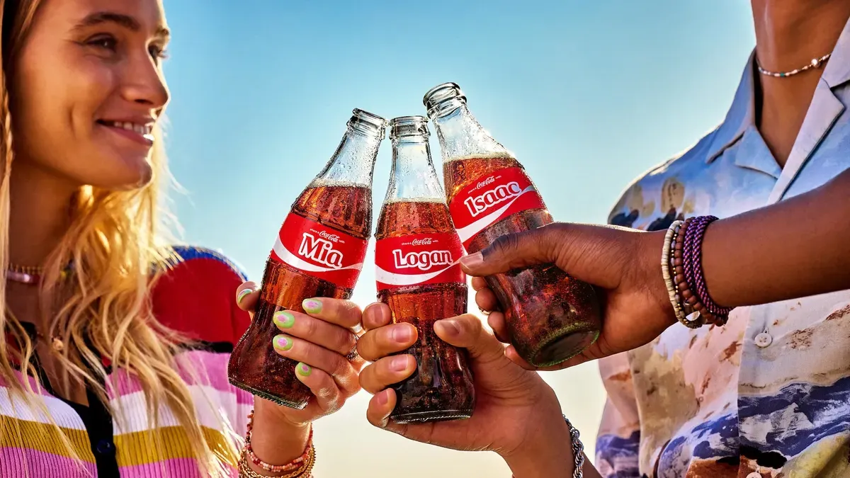 Three people cheers with Coke bottles emblazoned with names as part of the brand's 'Share a Coke' campaign.