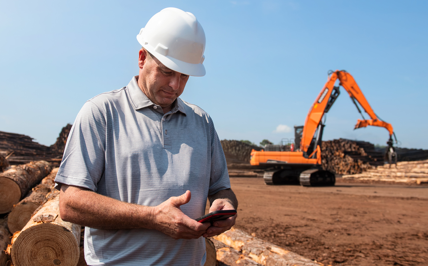 A crew member near a DEVELON log loader reviews telematics data on his phone.