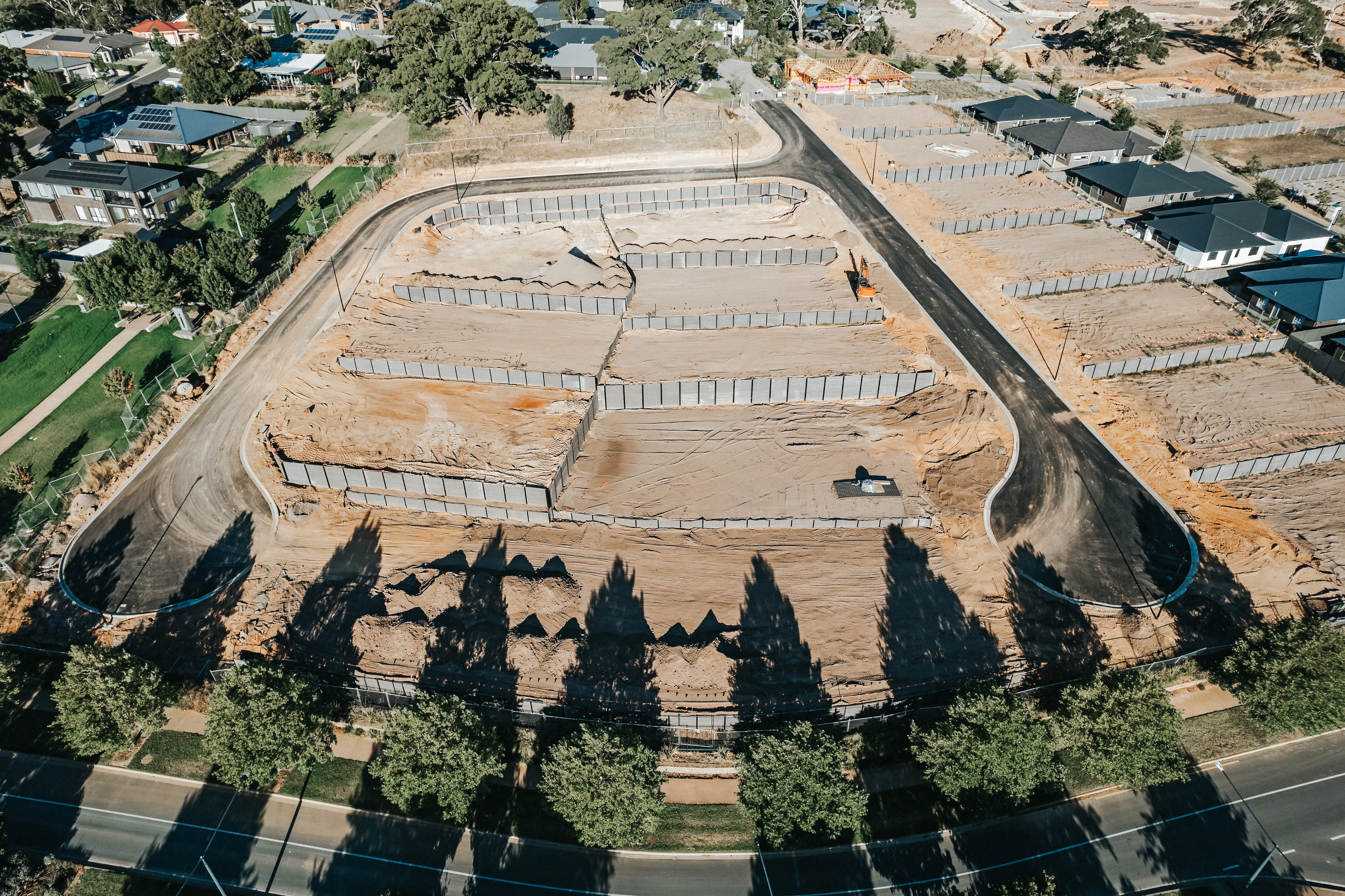 Aerial view of a cleared residential lot with outlined foundations and surrounding roads in a developing neighborhood. 