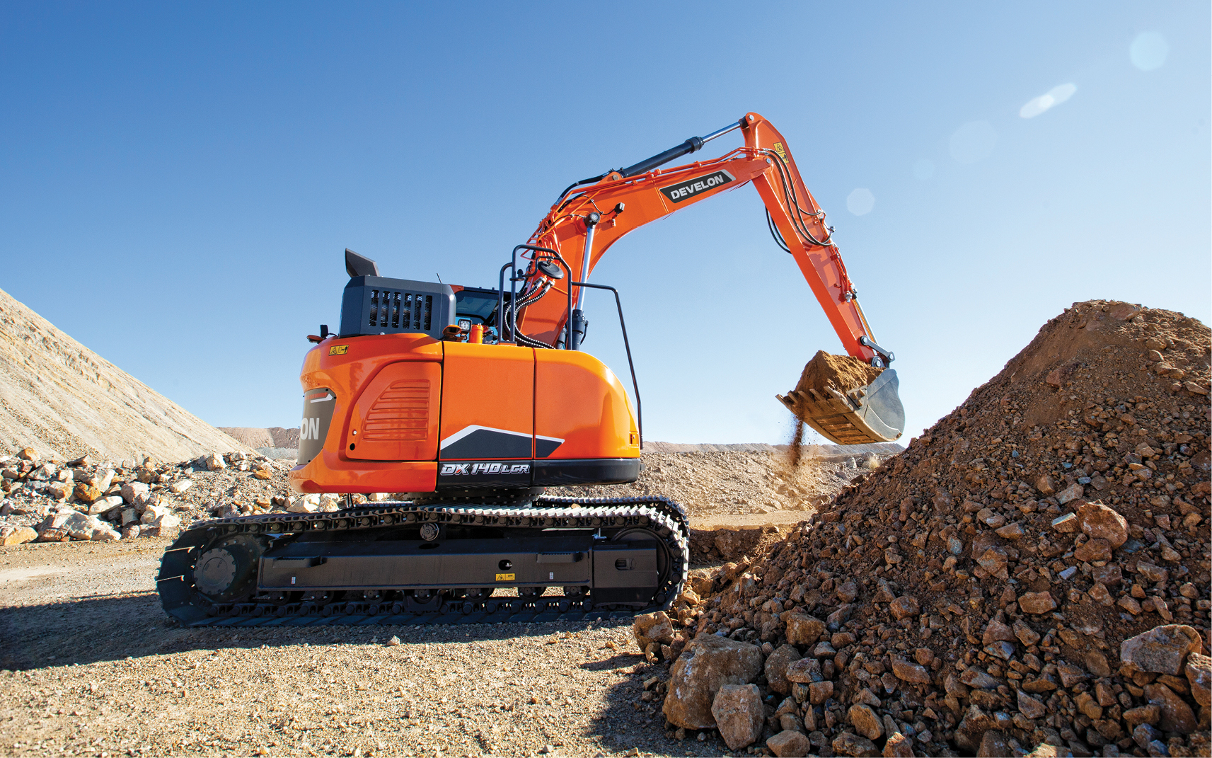 An excavator lifts a bucket of dirt and rocks at a job site.