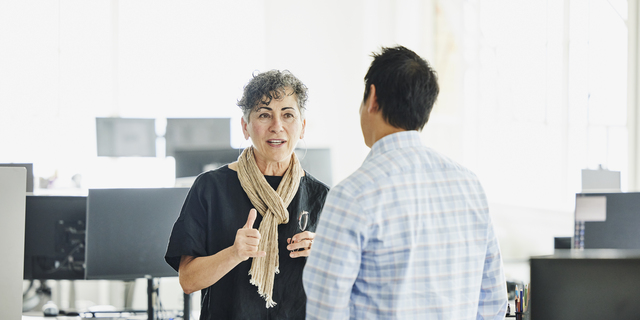 Medium wide shot business owner discussing project with colleague in office