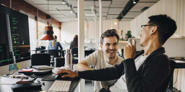 Happy multiracial computer programmers laughing while working at tech-startup office