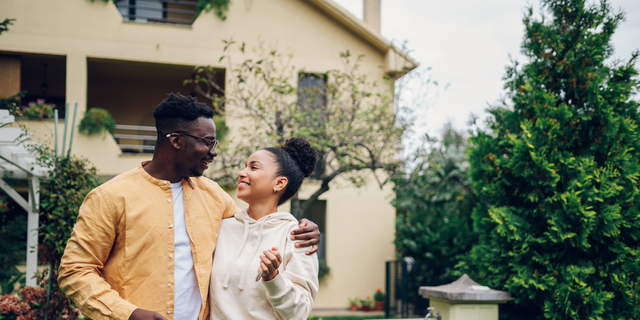 Multiracial couple holding keys and standing outside their new home