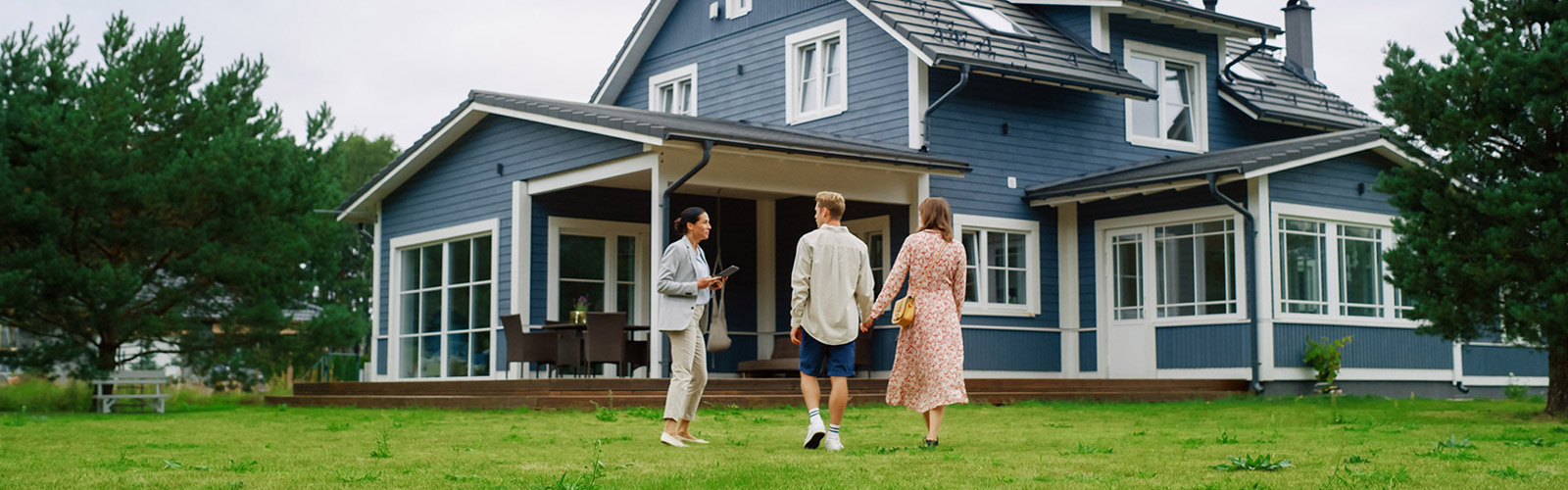 A woman in a suit and a man and a woman wearing casual clothes and holding hands talk in front of a blue house