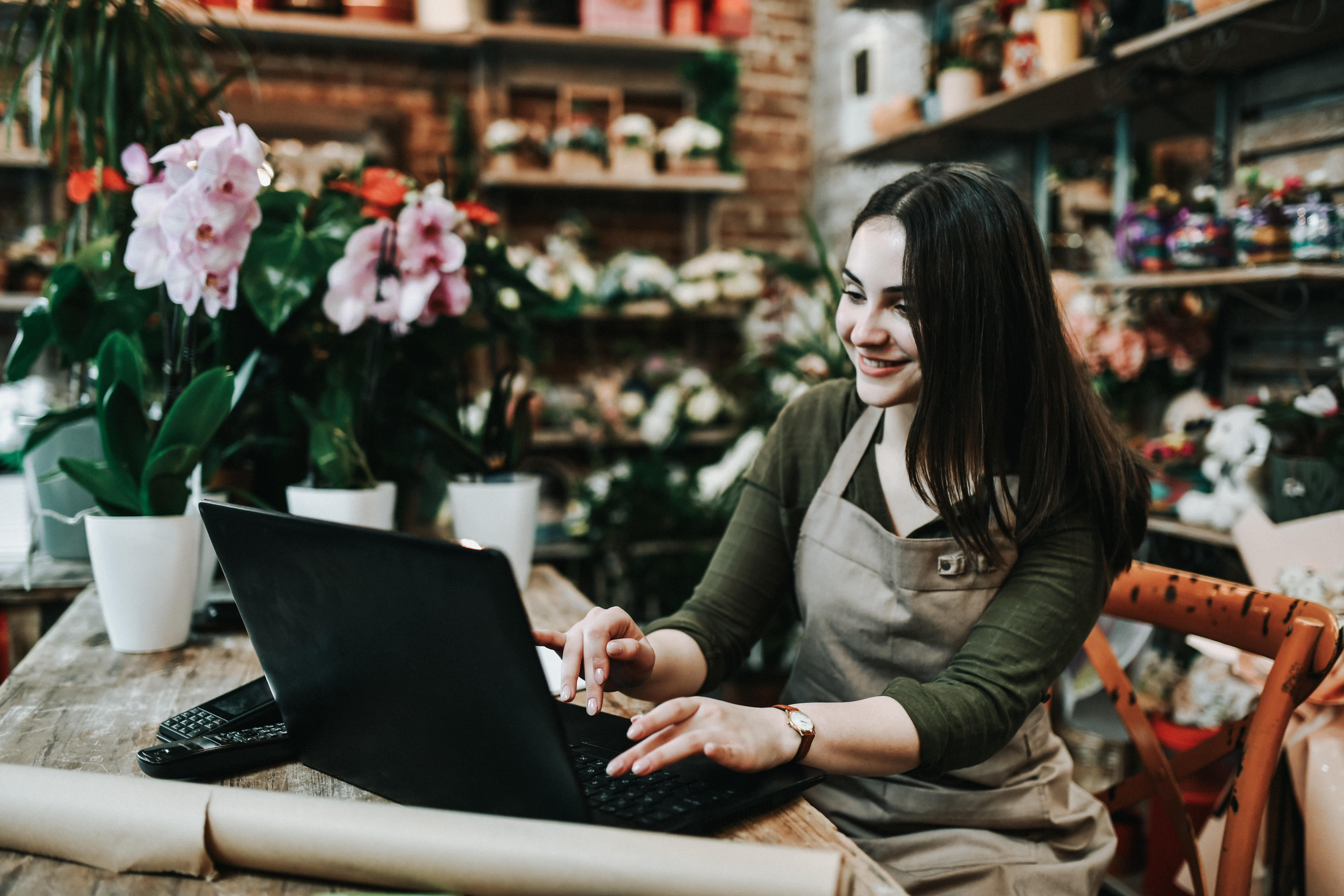 Smiling female small business owner sitting at laptop in apron 