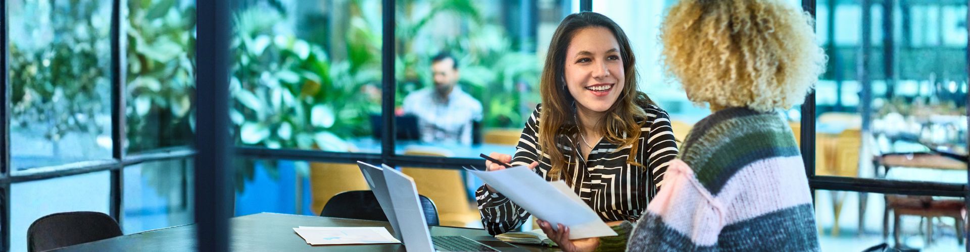Two women in a meeting using a laptop and reviewing paperwork