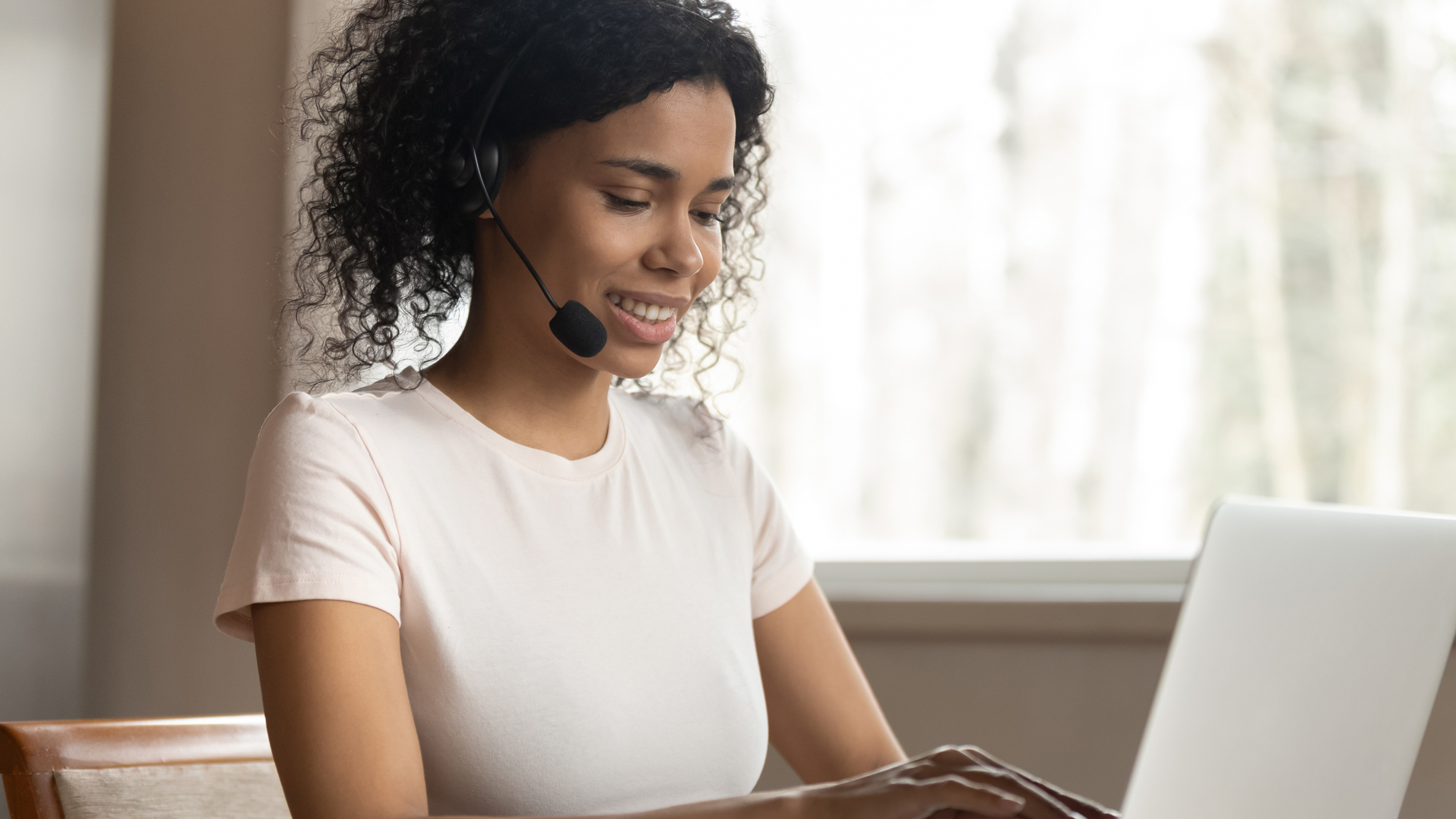 Young mixed race woman wearing headphones typing on computer