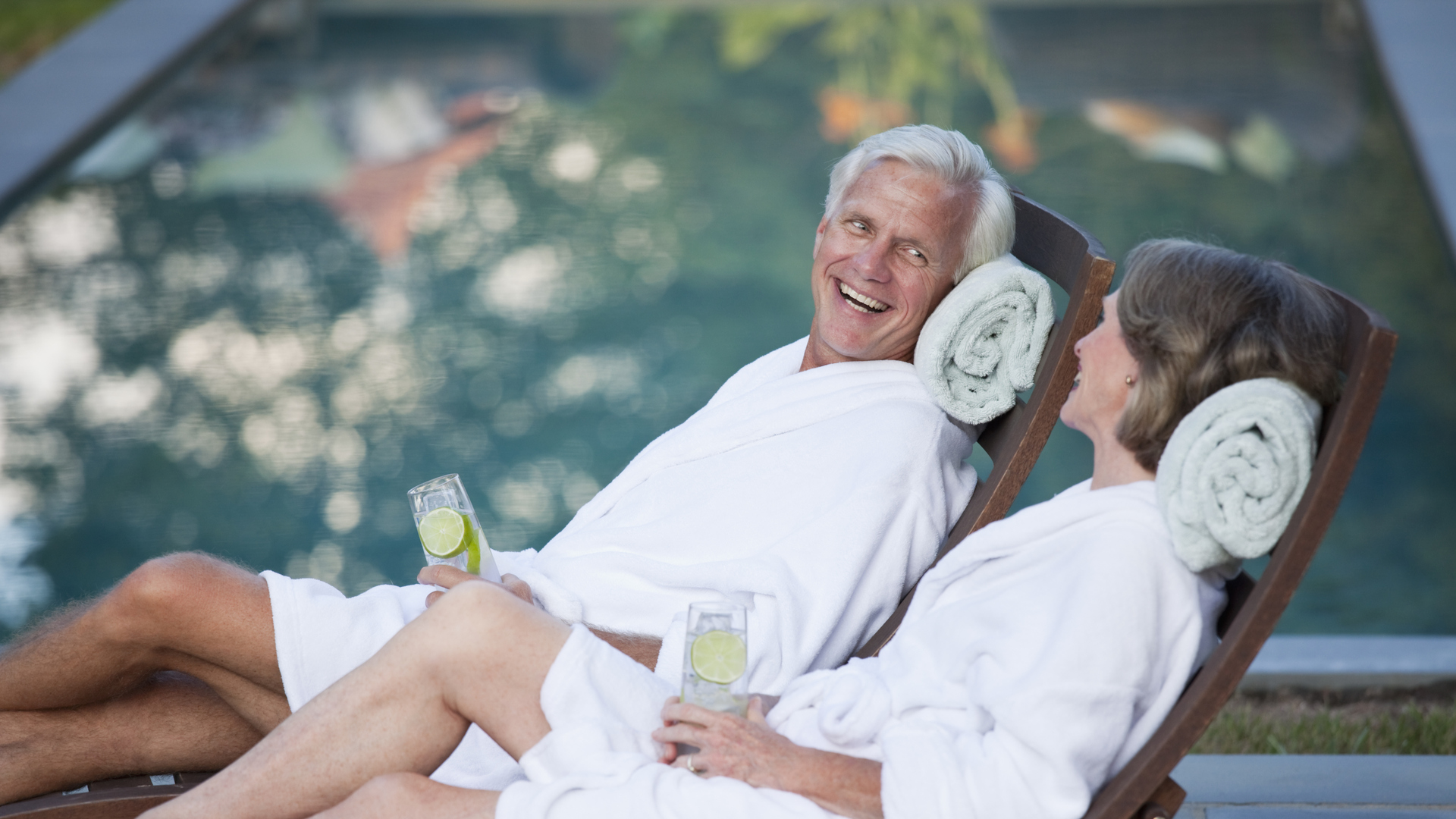 Couple in robes relaxing in lounge chairs at poolside