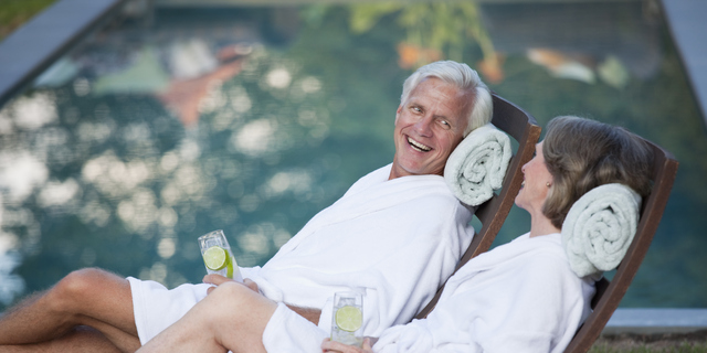 Couple in robes relaxing in lounge chairs at poolside