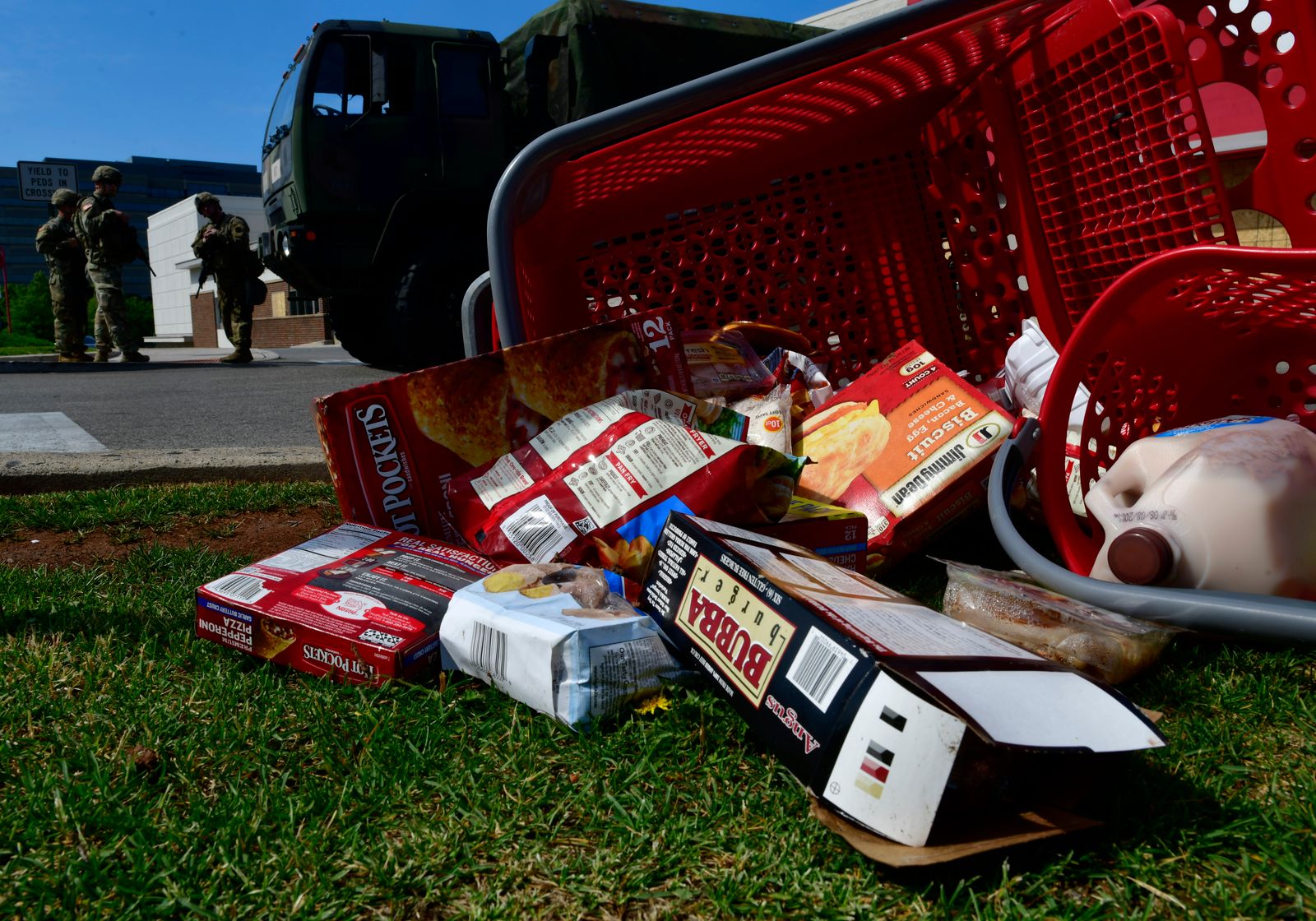 An overturn red shopping cart with food strewn on the ground