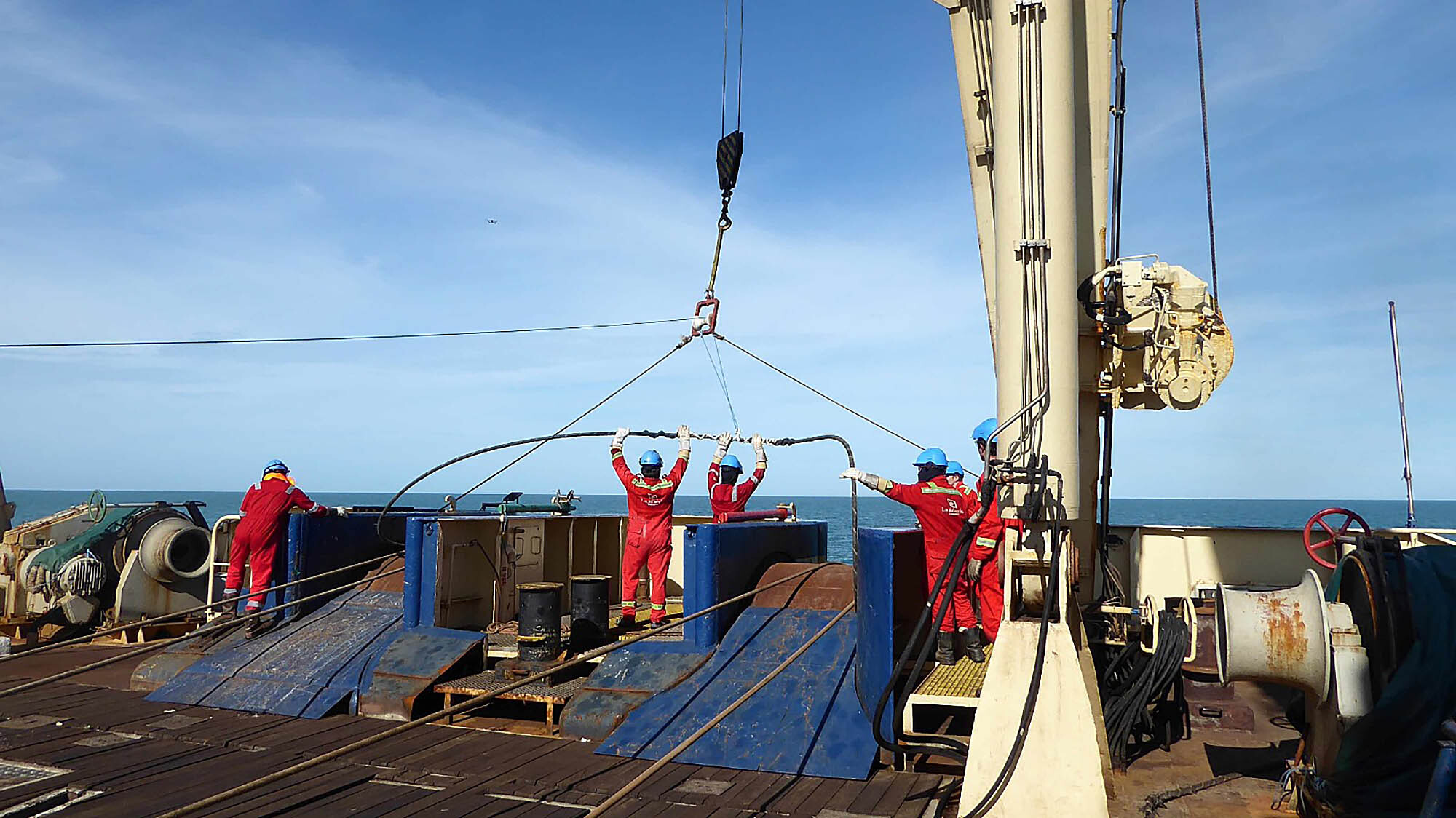 Image of six submarine repair workers aboard the Optic Marine guiding repair equipment