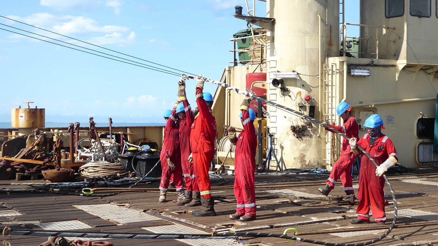 Image of six submarine repair workers aboard the Optic Marine guiding repair cables