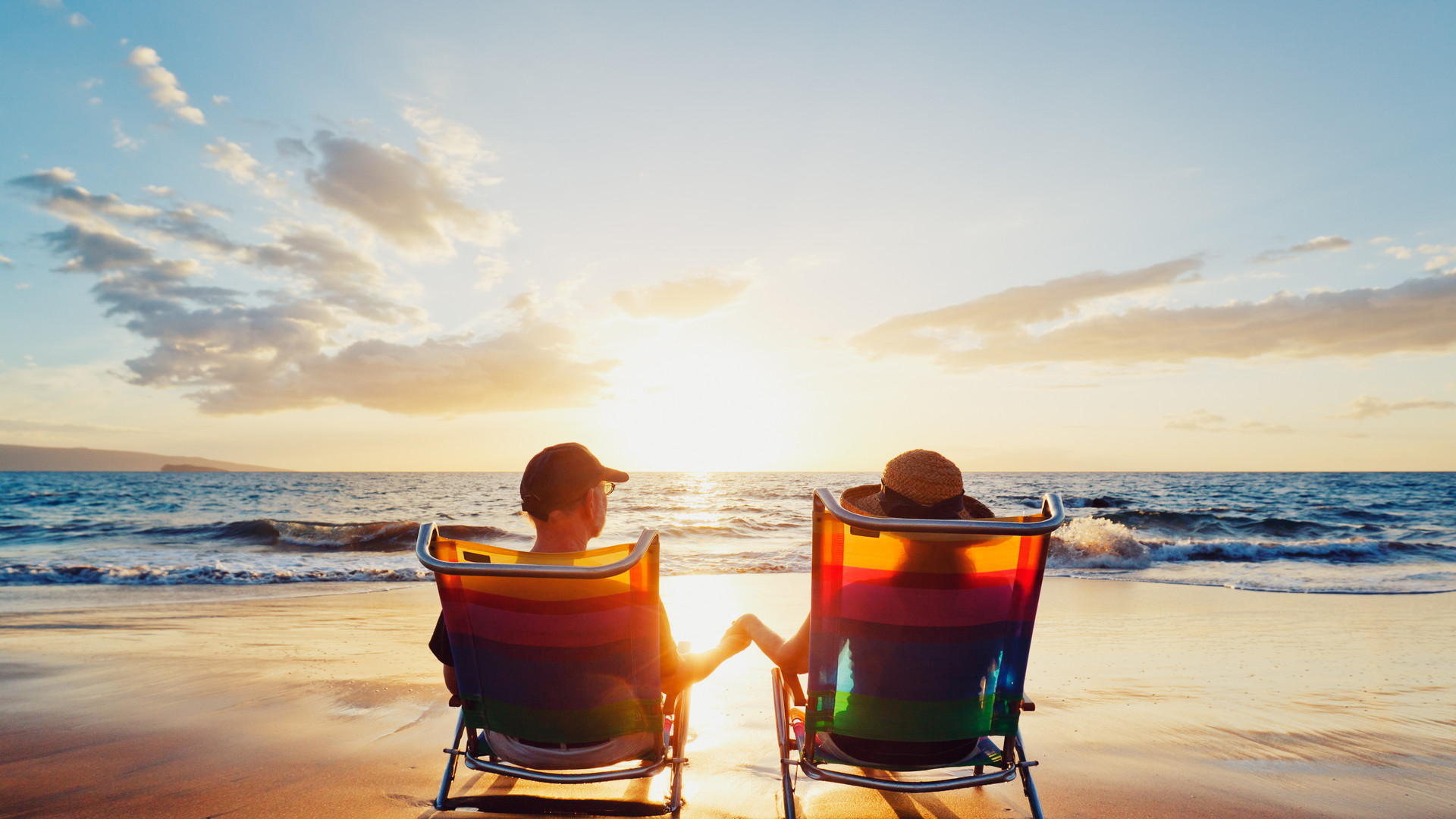 A couple, in beach chairs, holding hands at sunset