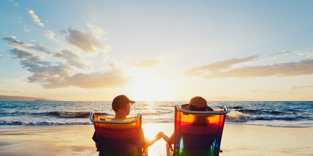 A couple, in beach chairs, holding hands at sunset