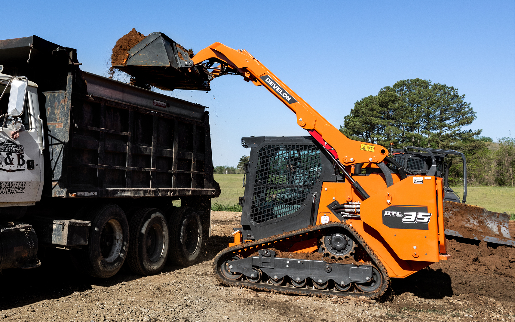 A DEVELON DTL35 compact track loader unloads dirt into a dump truck.