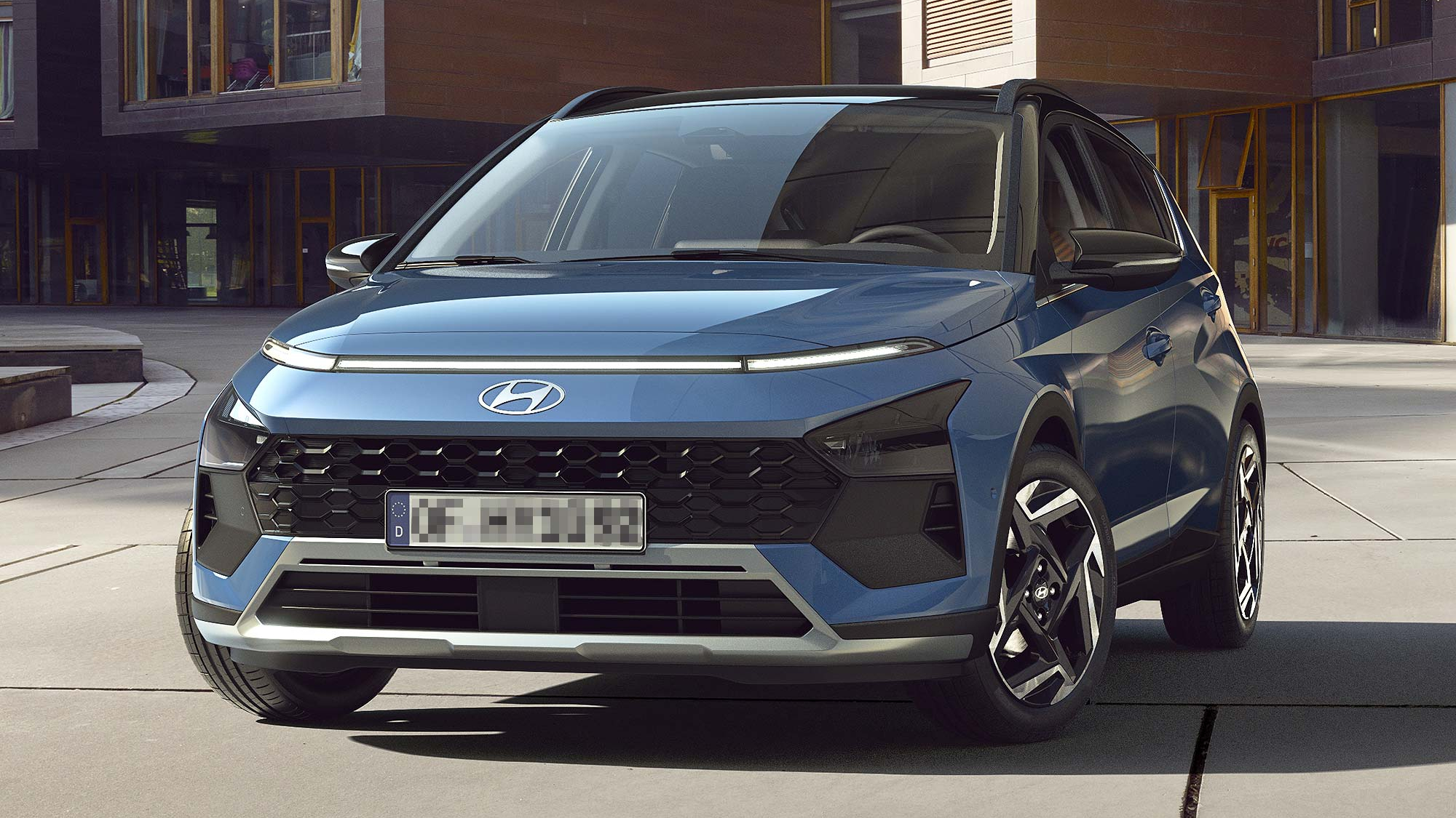 A blue Hyundai Bayon compact SUV parked in a modern urban courtyard, with sharp design lines and slim headlights.